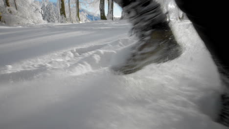Beine,-Die-Im-Winter-Im-Tiefen-Neuschnee-Durch-Den-Wald-In-Zeitlupe-Laufen,-Wobei-Viele-Schneepartikel-In-Der-Luft-Fliegen
