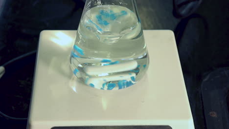 close up of blue crystals of copper sulfate pentahydrate being added to erlenmeyer flask on magnetic stirrer