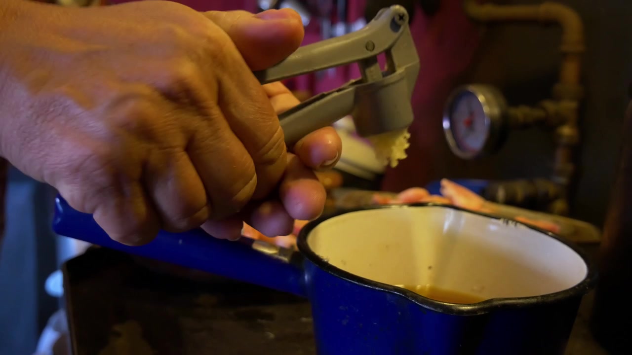 Close up Handheld Shot of Elderly Womans Hands Squeezing out Onion Into a Blue Pot in an Old Dirty Countryside Kitchen for a Cajun Dish With a Messy Background