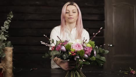 la florista encantadora presenta su trabajo, pone en la mesa un hermoso ramo de flores coloridas en largos tallos estables. bastante sonriente, gesticulando con las manos. vista frontal