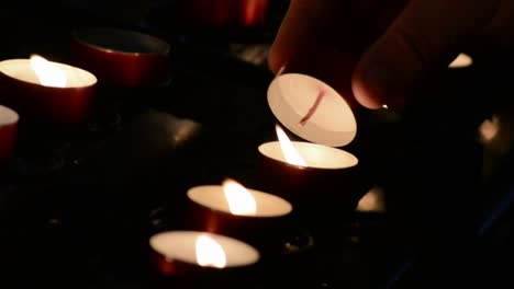 A-hand-lights-many-burning-red-candles-in-a-dark-church