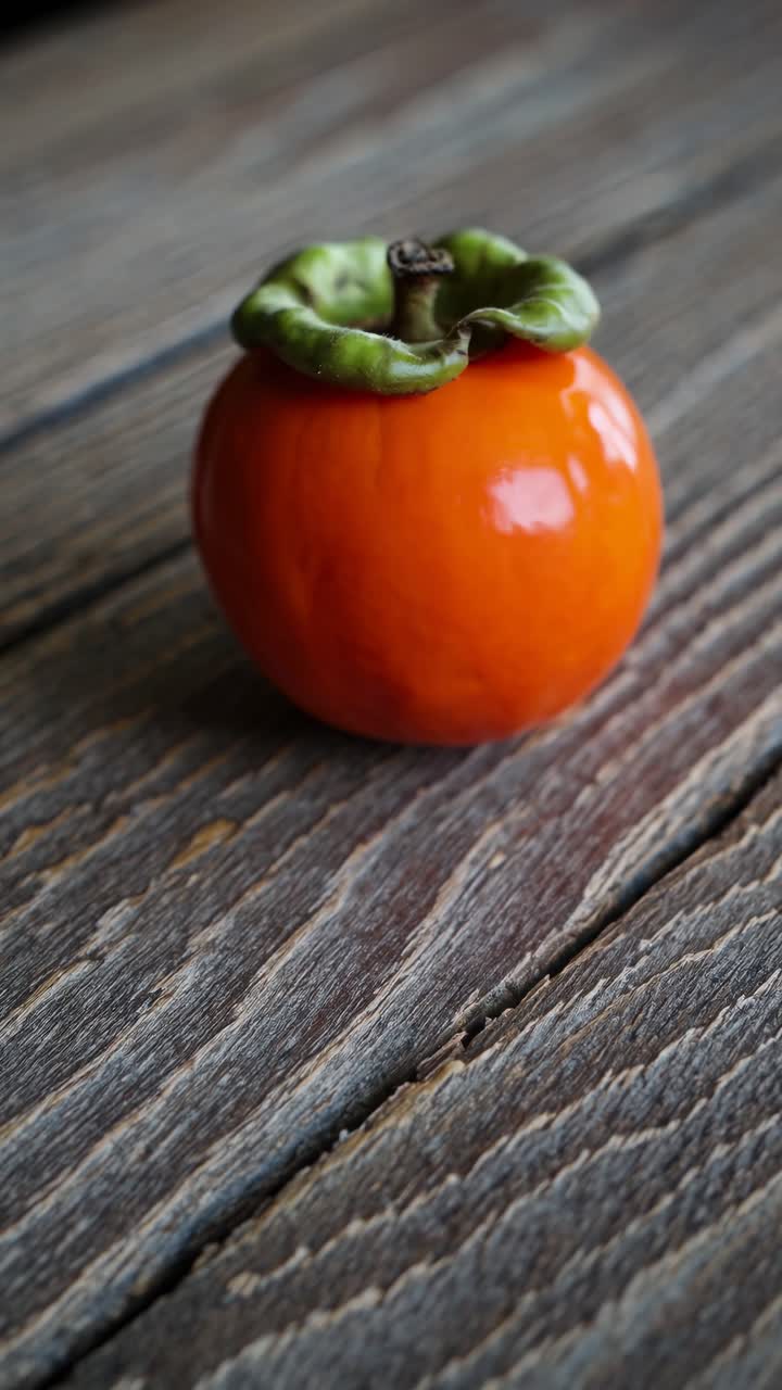 Close-up video shot of a vibrant persimmon on rustic wooden surface