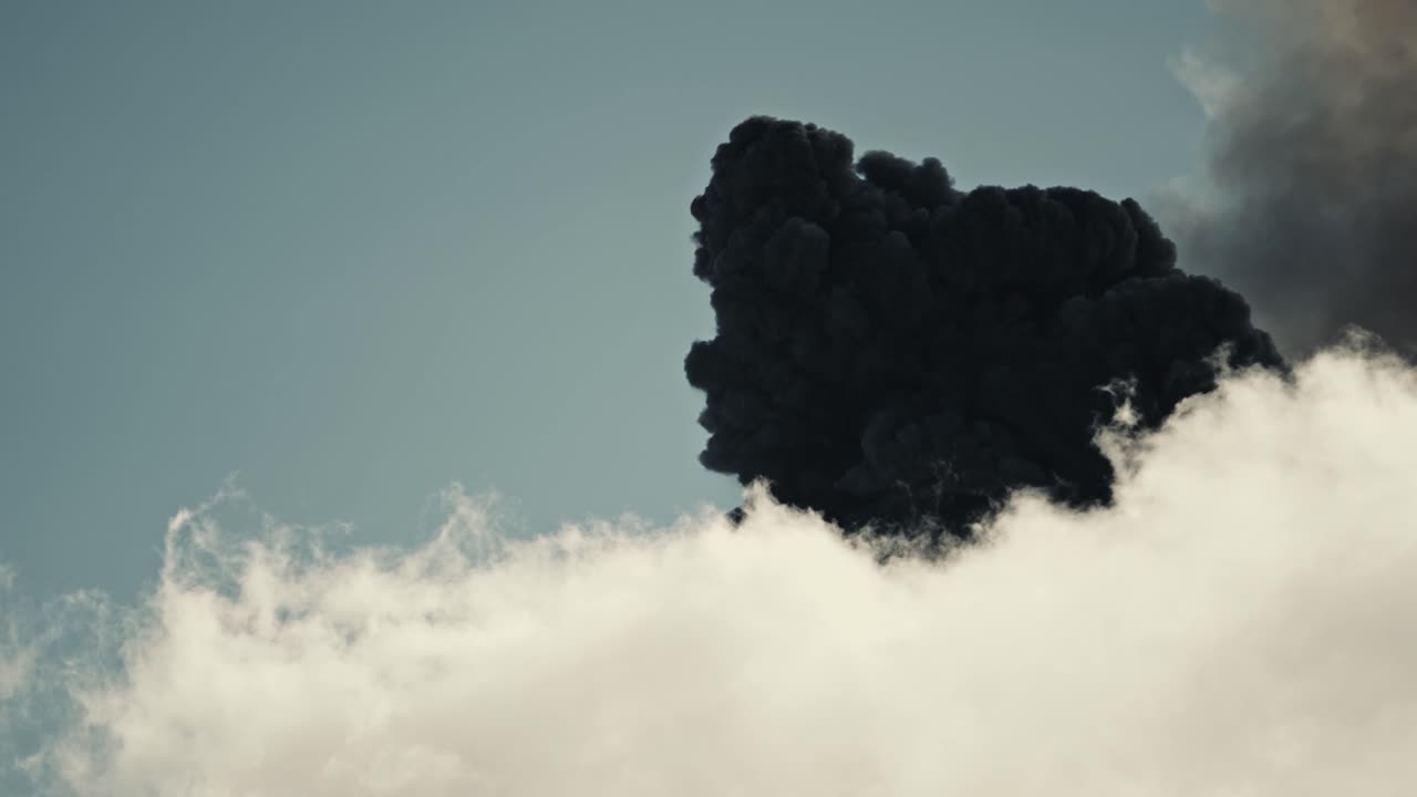 Dark smoke and ashes rise above white clouds, erupting Fuego volcano