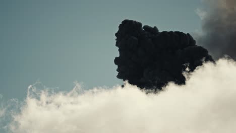 dark smoke and ashes rise above white clouds, erupting fuego volcano