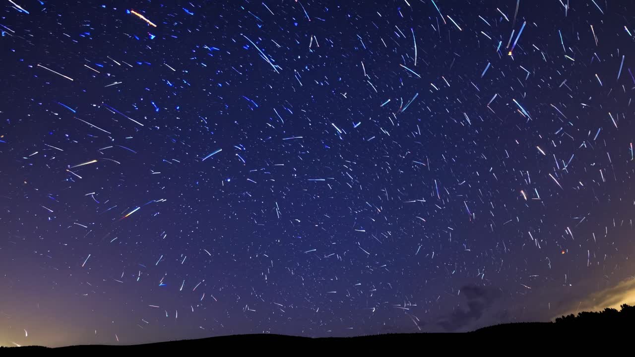 Time-lapse video of a starry night sky with streaking meteors, captured from a low-angle view