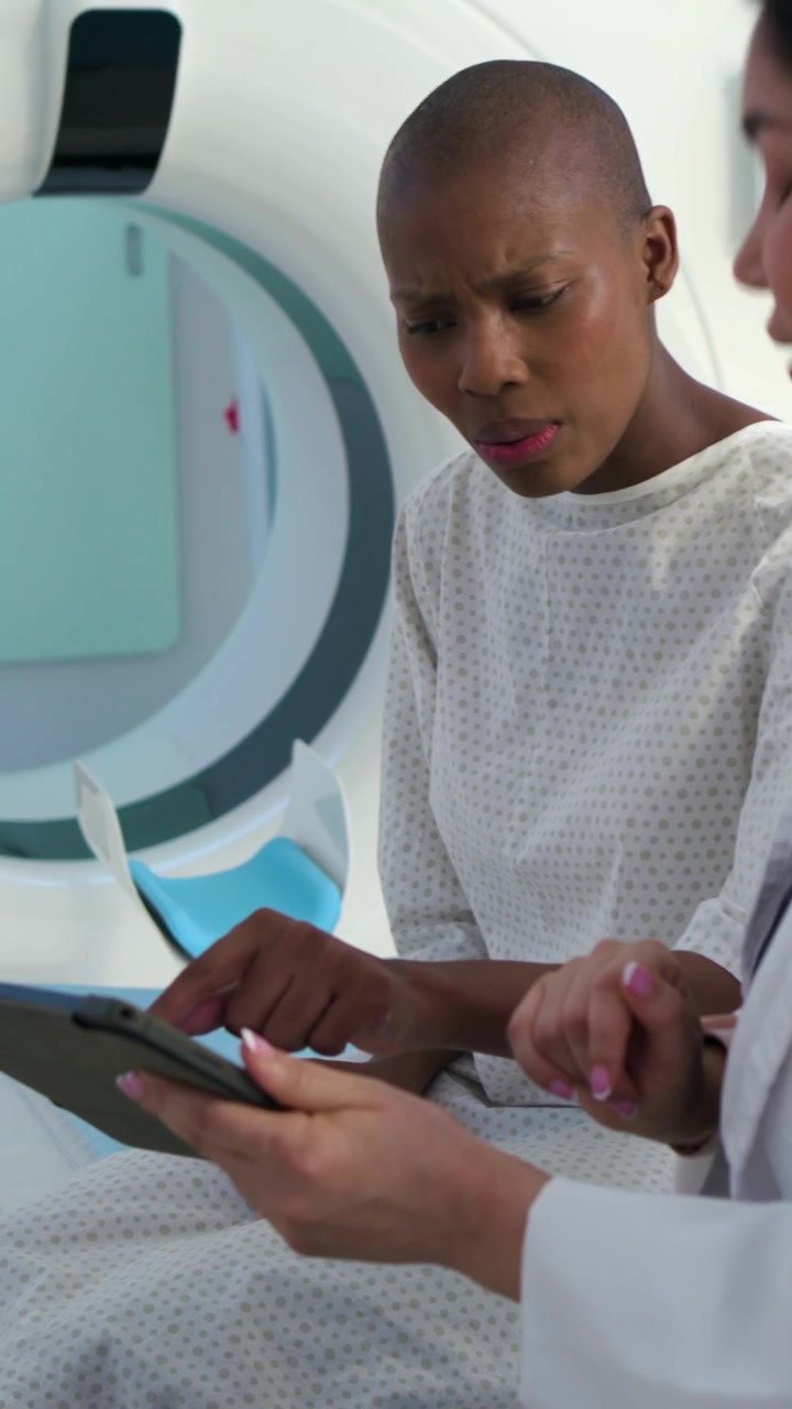 Vertical video: Reviewing woman in gown as doc in white coat tapping tablet for MRI prep at scanner