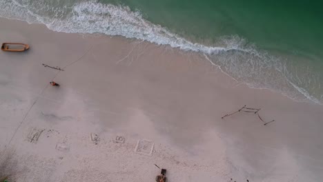 Motorbike-is-riding-on-white-sandy-beach,-sea-is-calmly-waving-the-shore,-4K-Beach,-Koh-Rong-Island,-Cambodia---aerial-top-down-view