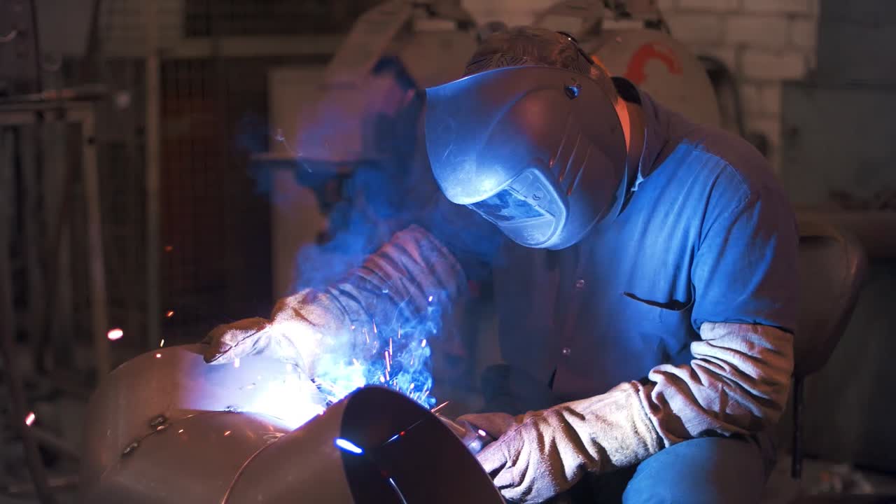 Industrial worker welding steel in protective mask at metalworking factory