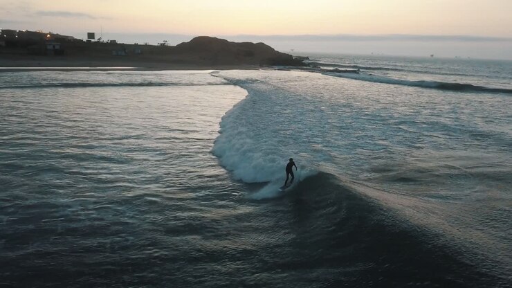 Drone aerial view of a surfer in the beautiful ocean of Peru during sunrise