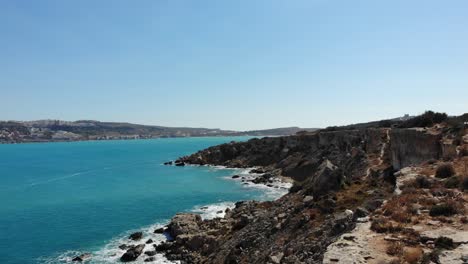 aerial forward horizon view of rocky cliffs, coast with calm blue sea in mellieha bay, malta