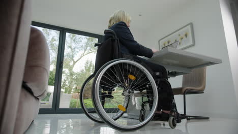 mujer en silla de ruedas en el escritorio de la oficina de casa desde atrás