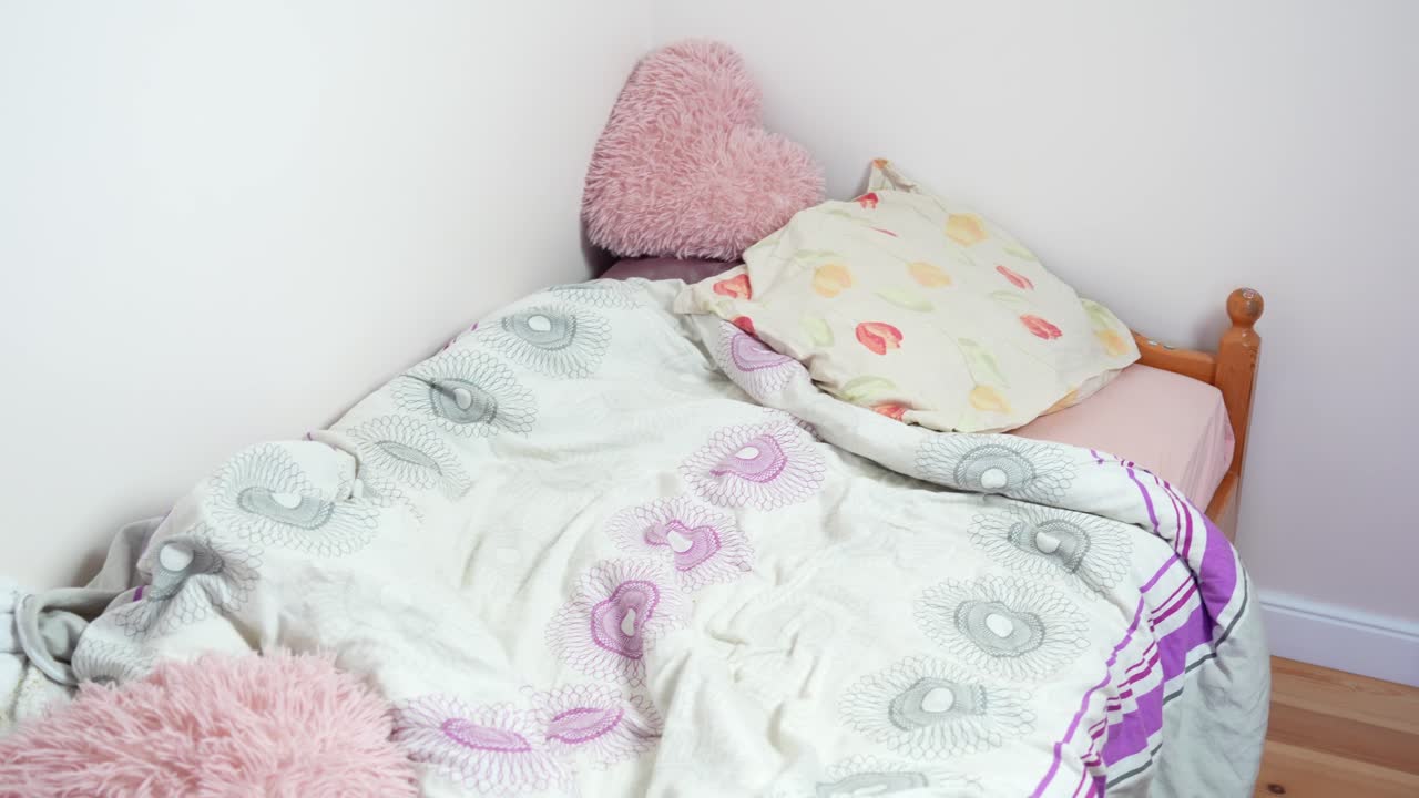 Letto di bambino disordinato con coperte sgualcite, cuscini soffici e una bambola nascosta tra i tessuti, visto dietro la sponda di un lettino di legno e un palloncino dorato in una camera da letto familiare realmente abitata