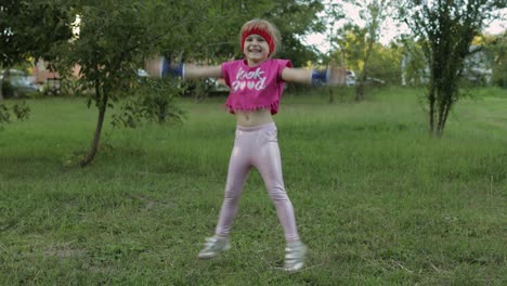 young cute child girl in sportswear making fitness jump exercises outdoors in park. workout for kids