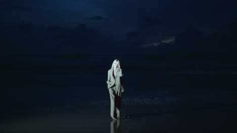 girl modeling night beach in light. relaxed woman in suit standing dark shore