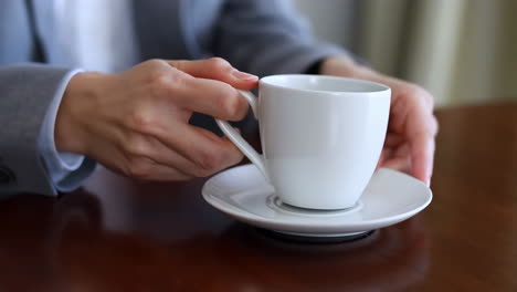 a person's hands holding a white coffee cup on a wooden table