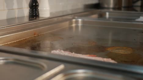 Chef-putting-fresh-delicious-bacon-on-hot-stove-for-cooking,-close-up-shot