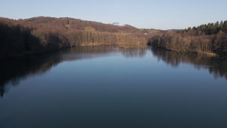 blue fresh water lake within a brown leafless forest on a bluebird day in germany