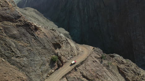 Cinematic-drone-shot-of-vehicle-on-Fairy-Meadows-Road-in-Pakistan,-second-deadliest-highway-in-the-world,-tracking-then-rotating-downward-aerial