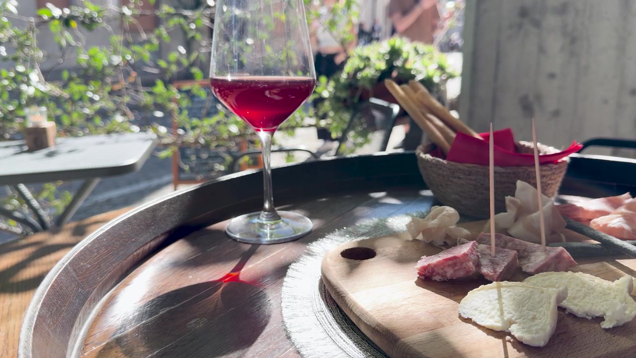 Un bicchiere di vino rosso si trova accanto a un tagliere di salumi su un tavolo esterno soleggiato
