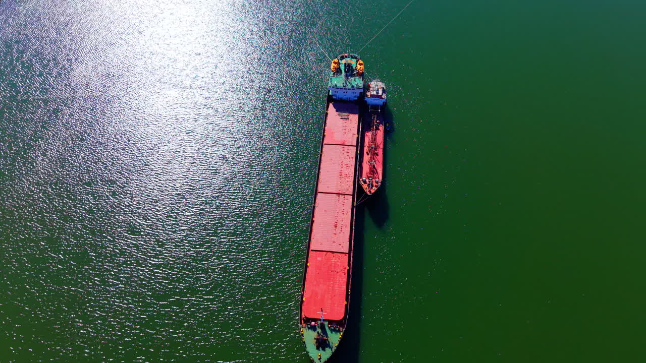 Operación de bunkering o transferencia de buque a buque en agua de mar verde con destello solar. Vista aérea de un pequeño buque cisterna junto a un gran carguero.