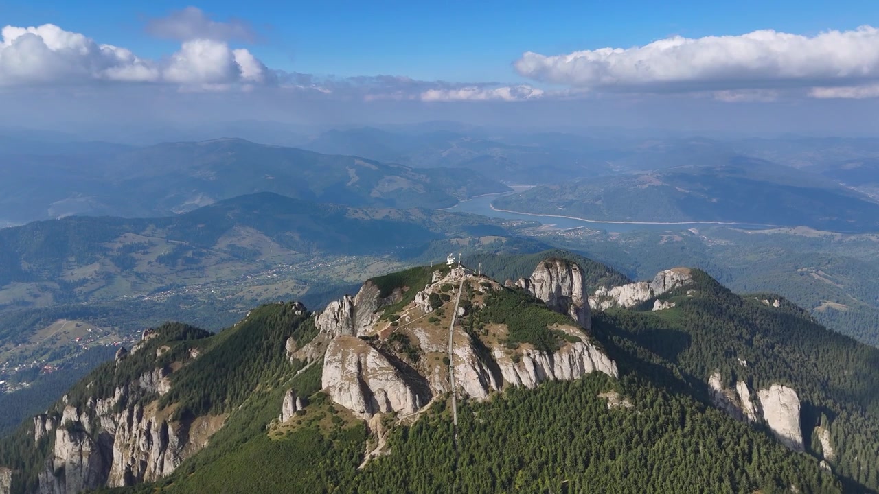 Drone voa sobre o pico Toaca com escada e antenas visíveis.