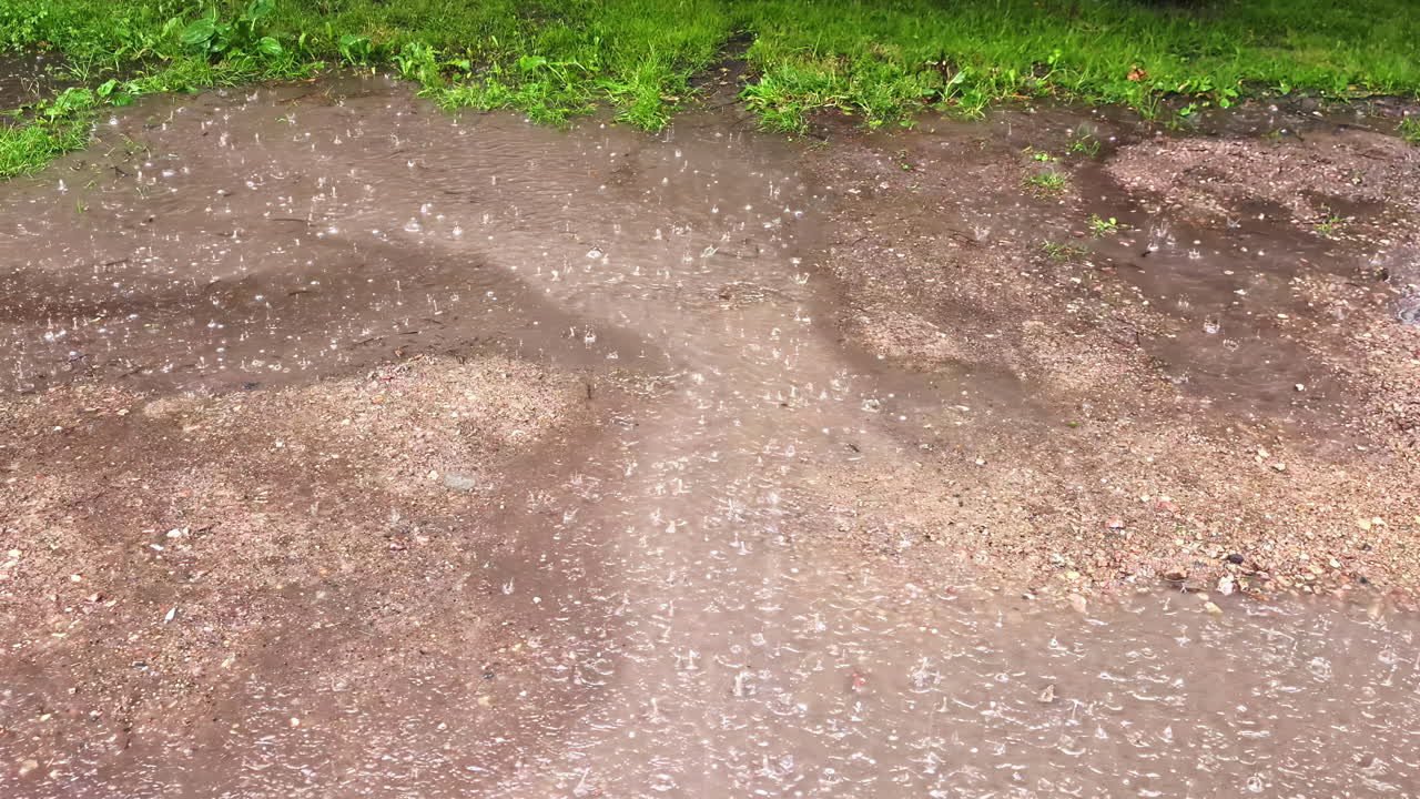 Close-up of rain falling in slow motion on cracked sidewalk and mud patches