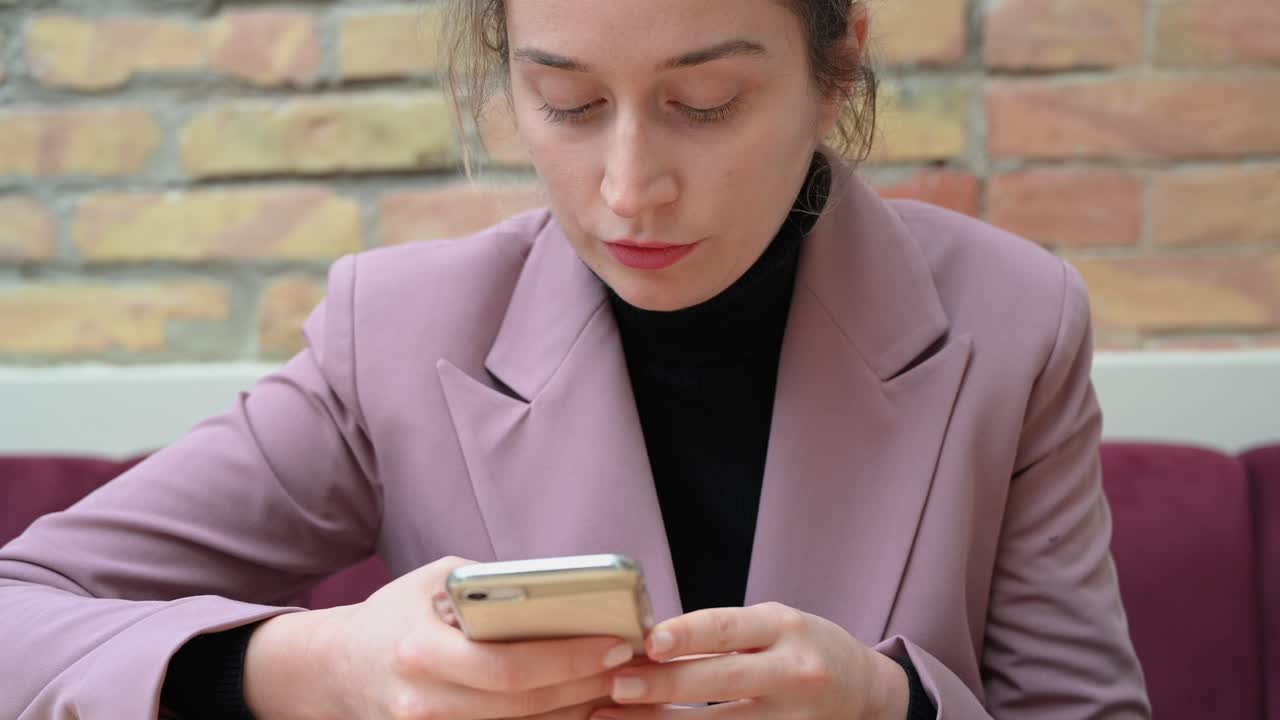 Close up of a woman in a pink blazer typing on her phone in a restaurant