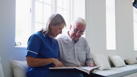 nurse and senior man sitting and looking at a book together