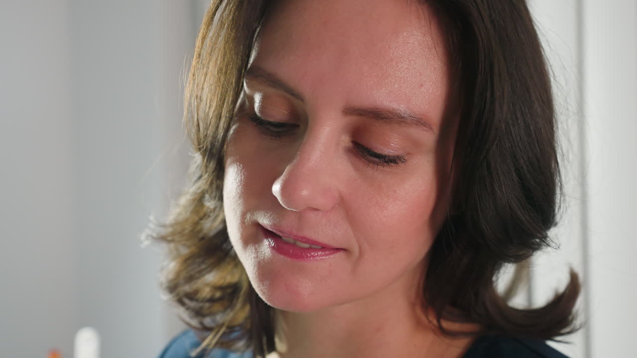 Close up of aesthetician face illuminated by bright studio lighting, eyes focused downward while performing cosmetic procedure, showcasing concentration, professionalism and calm demeanor