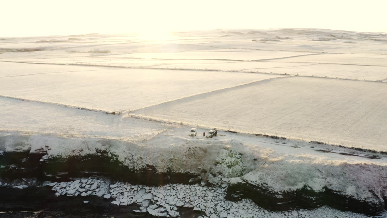 amigos se reúnen en el borde del acantilado en coches mirando hacia abajo en las rocas cubiertas de nieve que conducen al océano
