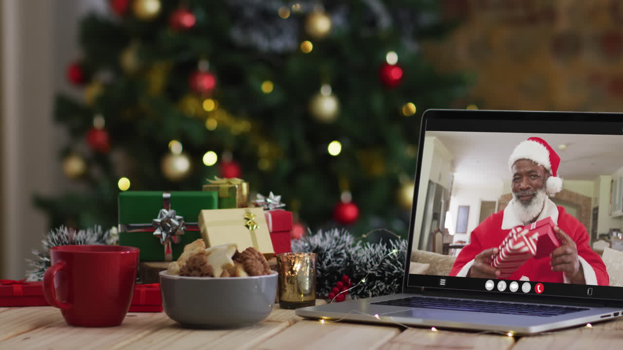hombre afroamericano senior en disfraz de santa en videollamada en computadora portátil, con árbol de navidad