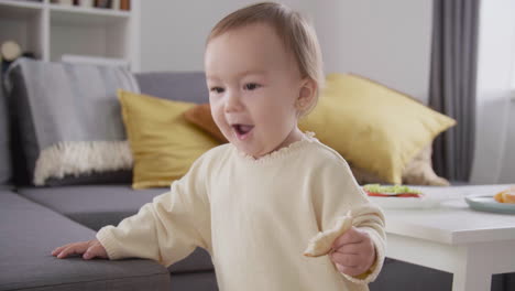 linda niña comiendo pan mientras está de pie junto al sofá en la sala de estar 2