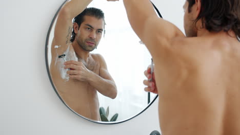 man shaving underarm in front of mirror