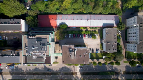 Top-down-static-aerial-ower-building-and-street---cars-move-slowly-around---close-up-green-trees-and-roof-top