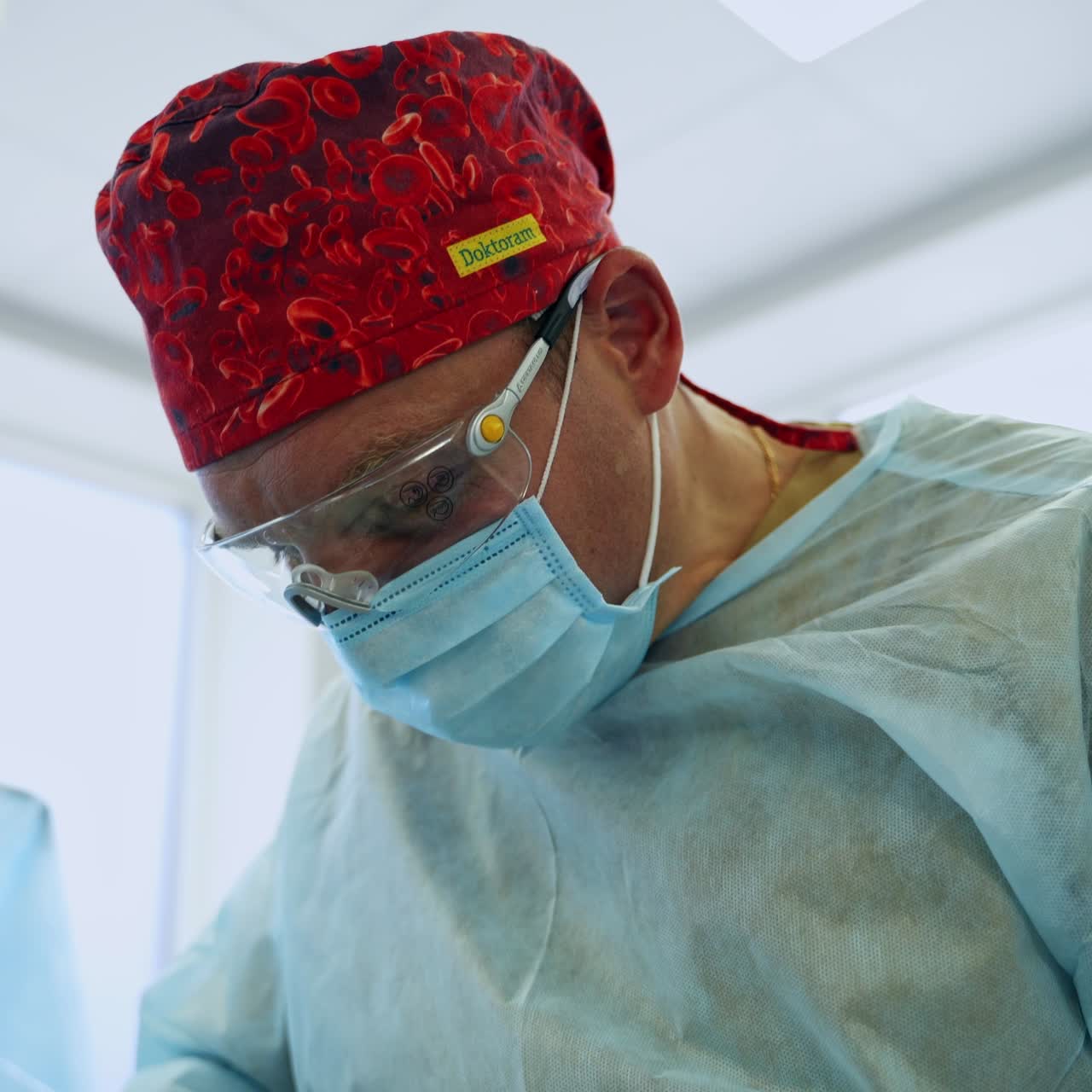 Adult male doctor wearing red hat, mask and glasses for surgery. Portrait of a experienced surgeon busy at operation from low angle view