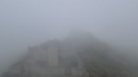 a drone rises above castle marvão through the thick mist