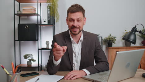 Businessman-working-on-office-laptop-pointing-to-camera-looking-with-happy-expression-making-choice