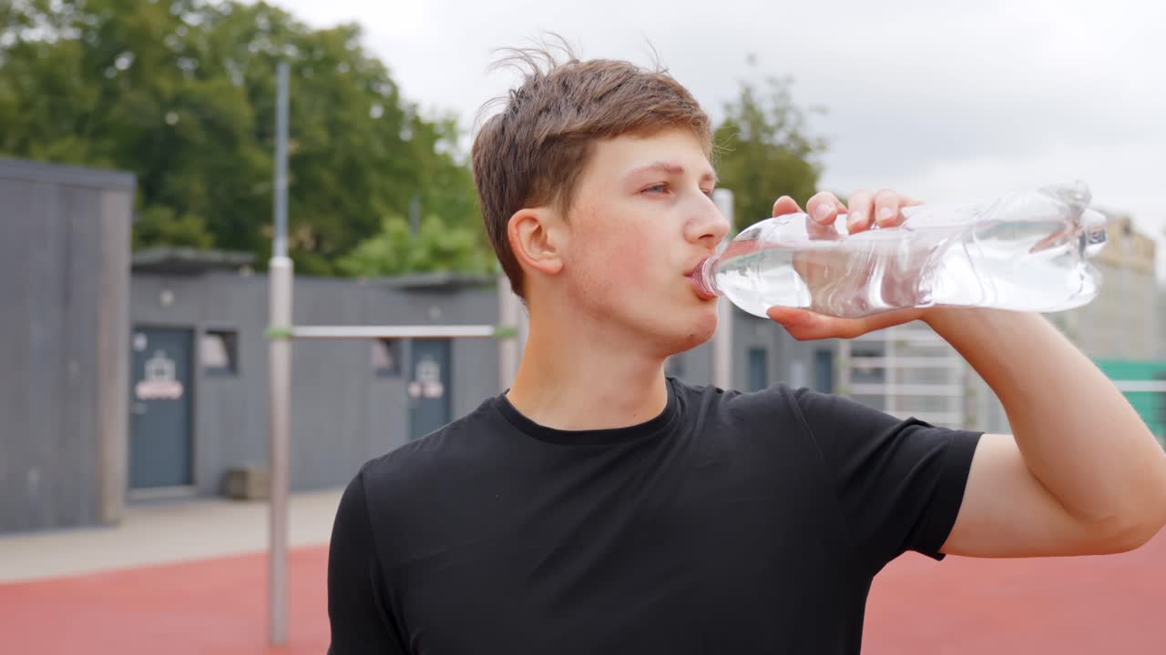 Young man in sportswear drinks water from bottle after workout, casual recovery moment