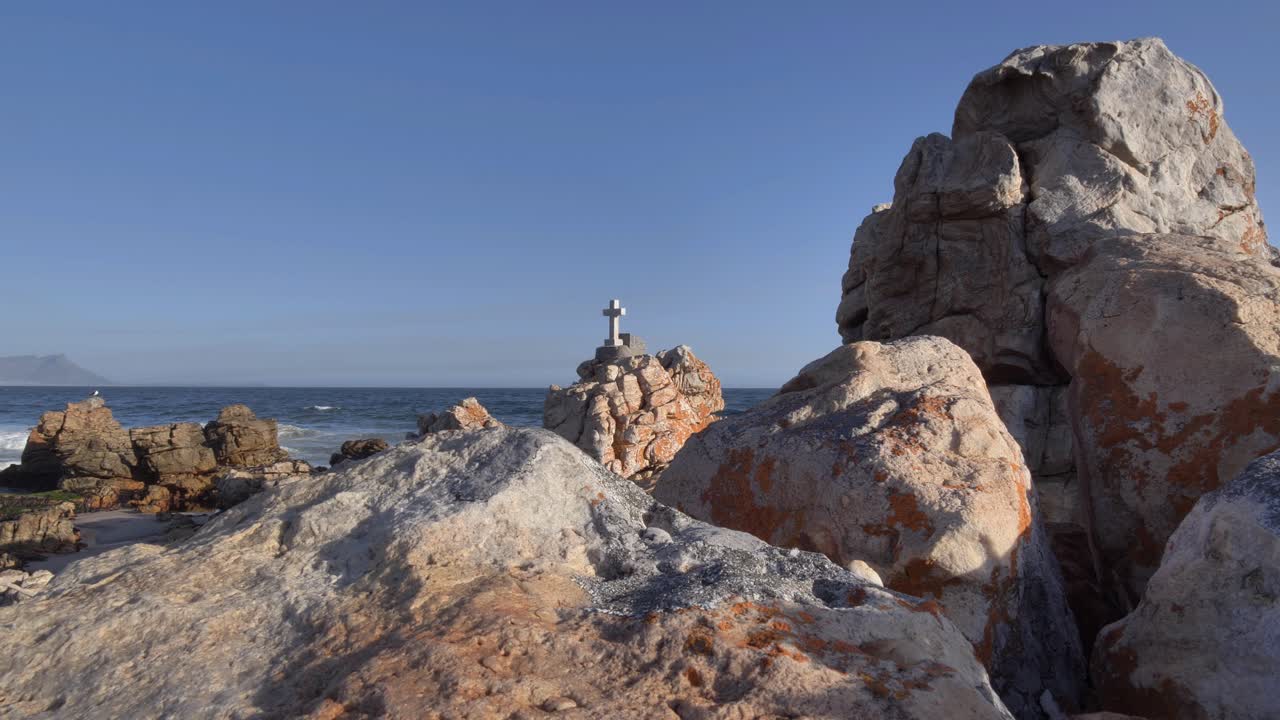 Croce di marmo si erge su una costa rocciosa mentre un gabbiano osserva contro l'orizzonte blu a Kleinmond, Capo Occidentale