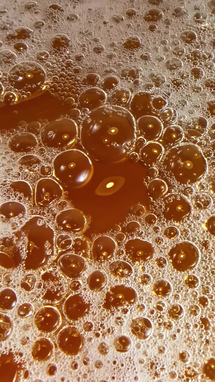 Vista de cerca de burbujas de cerveza efervescentes y espuma en movimiento, formando un fondo líquido dorado dinámico