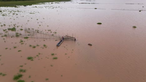 aerial flyover fishermen in boat attend to arrow head fishnet traps along the brown muddy flooded waterways of the mekong delta