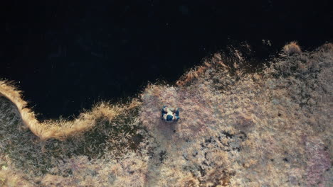 AERIAL-TOP-DOWN---A-man-sits-by-a-frozen-lake-in-easy-pose-before-an-ice-bath