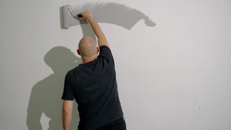 A-man-is-painting-a-wall-gray-with-a-roller,-shot-from-behind
