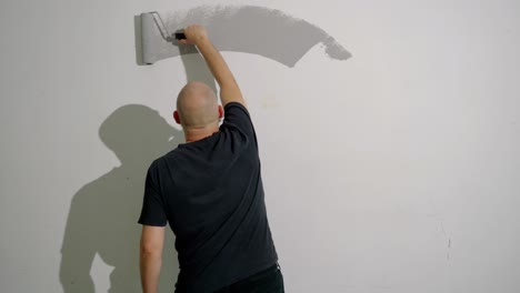 Un-Hombre-Está-Pintando-Una-Pared-Gris-Con-Un-Rodillo,-Disparado-Desde-Atrás