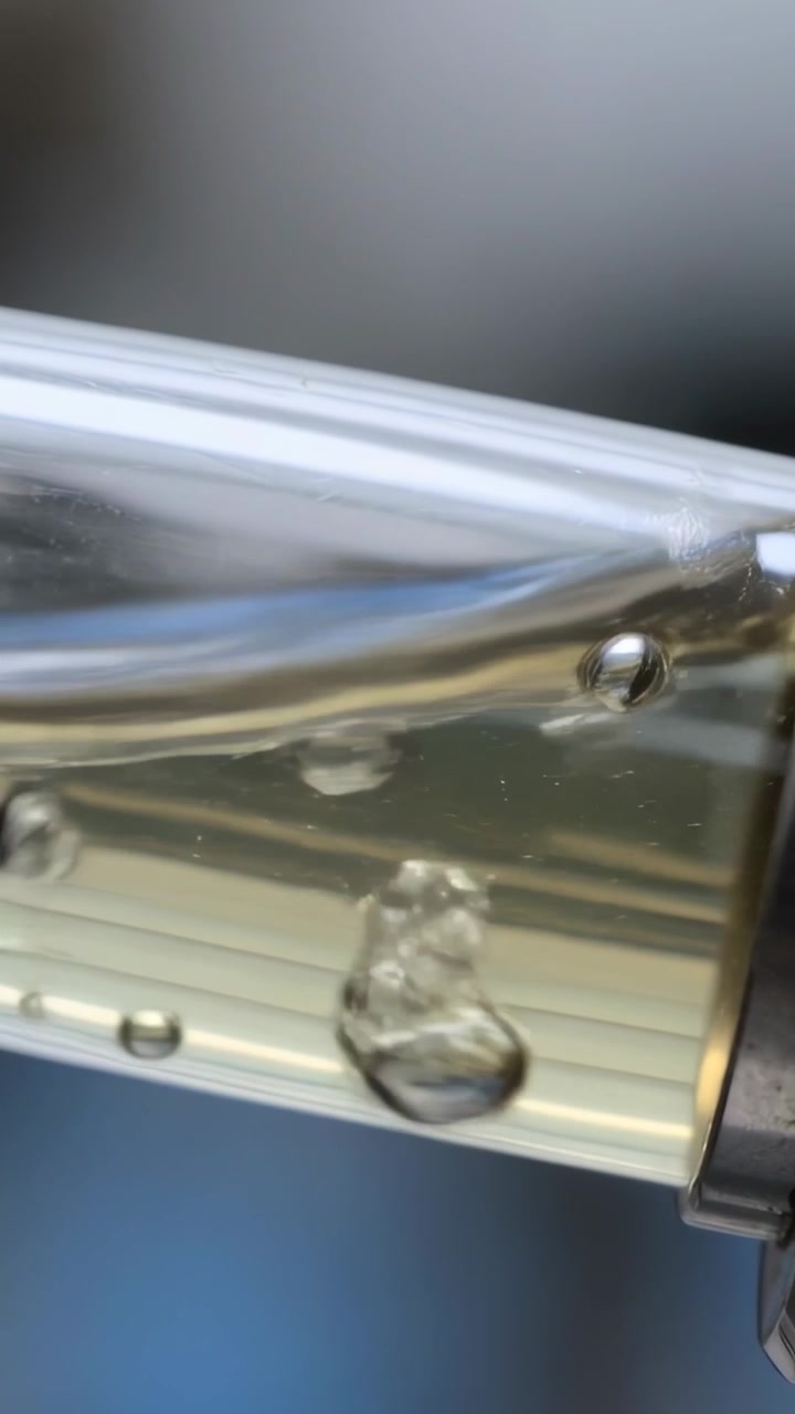 Vidéo verticale : Bulle se détachant d'une paroi et montant dans un tube en verre, dans un laboratoire avec un liquide pâle et un rivet.