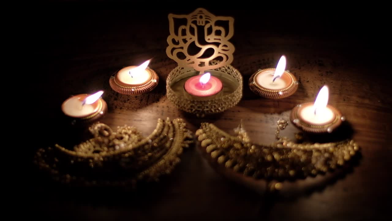 Worshiping of ornate golden bridal wedding and ceremonial jewelry with blessings from Lord Ganesha cutout sculpture among diys candles for Diwali, Hindu festival of lights.