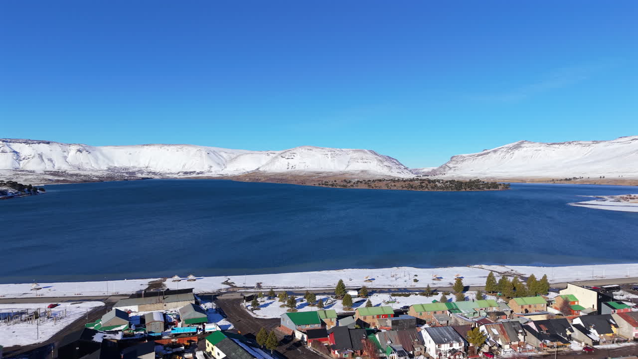 Snowy coastal Caviahue village beside the calm blue Lago Caviahue water bay in winter season, Neuquén, Argentina