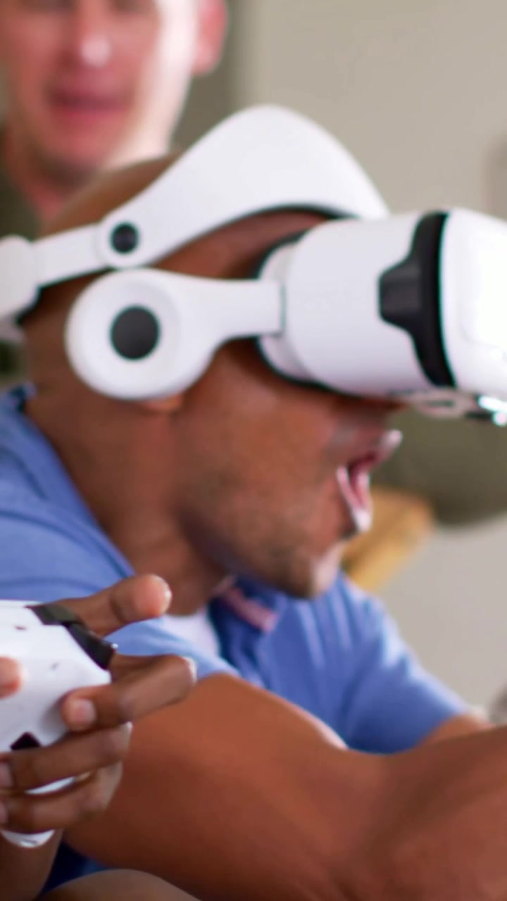 Vertical video: Reacting to game man in blue shirt with white VR headset on couch, holding gamepad