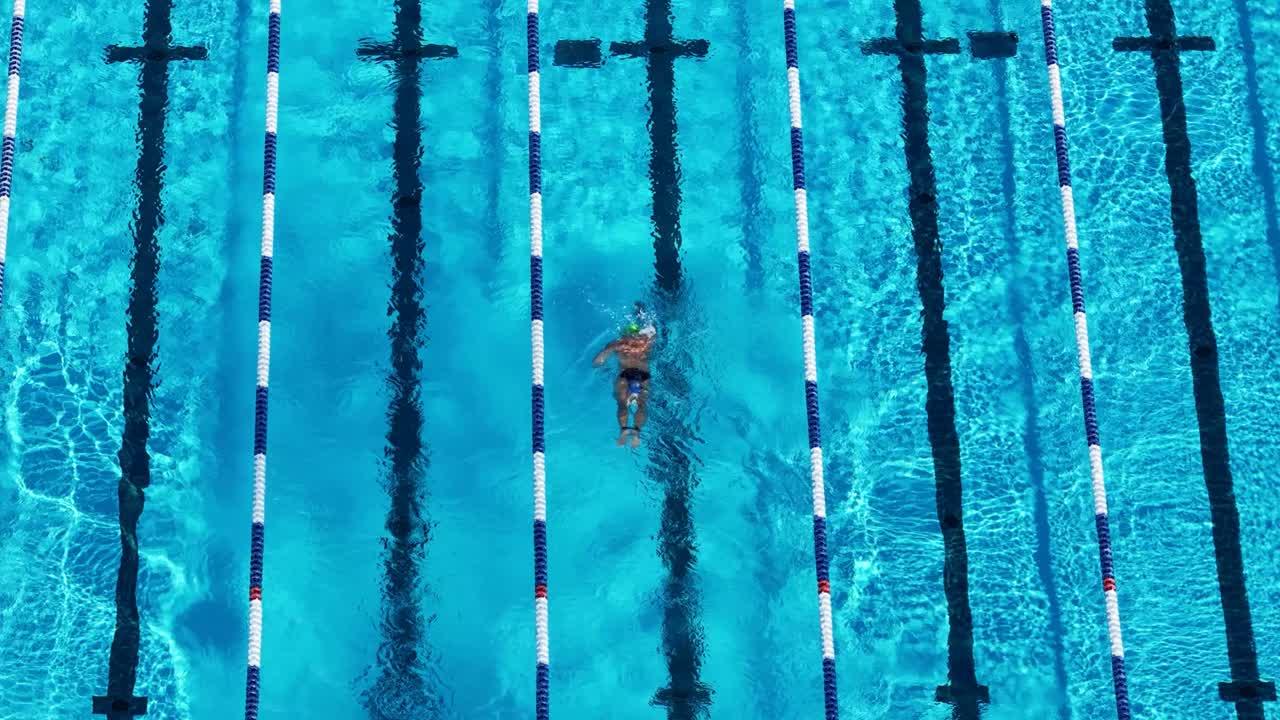 Drone captures swimmers practicing freestyle in a sunlit pool. Vibrant blue water and lane lines create dynamic patterns