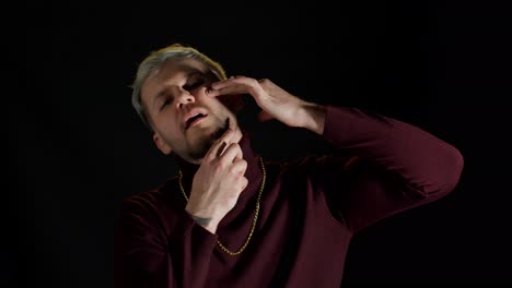 Portrait-of-unshaven-young-man-in-trendy-stylish-clothes-shaving-with-knife-against-black-background